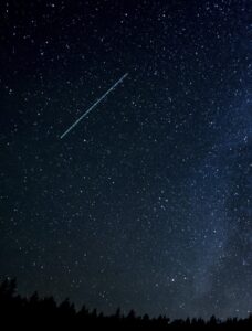 A shooting star shoots across a star-filled night sky.